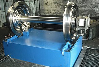Hub- Rollvorrichtung; feste Spurweite Hub-Rollvorrichtung für eine feste Spurweite mit Radsatz: Auf der Vorrichtung befindet sich ein Radsatz. Man kann nur den oberen Teil der Vorrichtung sehen, da die Hub-Rollvorrichtung bauseits in eine Grube eingelassen ist.