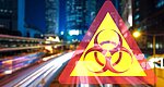 Large city shot as a blurred background. In the foreground, a triangular yellow traffic sign with a red frame and a biohazard symbol in the centre