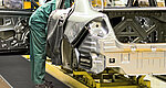 A worker in a green suit leans into a car body shell