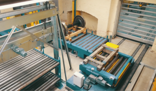 Removal wheelset and supply of further empty pallet: On the left in the picture ou will find the pallet magazine above the roller conveyors. The transfer car transports an empty pallet from the pallet magazine to the other building. On the heavy-duty roller conveyor, which is located next to the pallet magazine, a pallet with wheelset is transported.