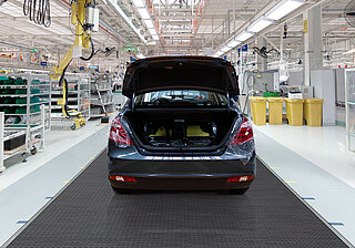 A car with an open boot is parked in a production plant