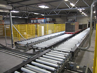 Storage -  Conveyor line for molds:  The molds are placed on top of each other and transported, buffered and stored in stacks. On the picture there are 3 roller conveyors arranged side by side. On the middle roller conveyor there are mold stacks. In the lower image area there is a rail-bound transfer car to ensure the supply of mold stacks to the individual conveyor lines.