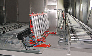 Tilting car for transport frames:   The tilting car (with roller conveyor) is a special construction that allows the transport frame to be turned by approx. 80° and then transferred to a vertical support roller conveyor (inclination approx. 80°). On the picture there is the empty tilting car (turmed by approx. 80°). On the right,  next to the roller conveyor, the vertical support roller conveyor can be seen on the wall (inclination approx. 80°)..