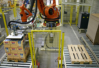 Palletizing robot for different packing patterns: On the right side of picture there are conveyor sections for the feeding of empty pallets and intermediate or bottom sheets. On the left side there is a roller conveyor, on which the products were stacked by the pictured articulated-arm robot according to a predetermined stack formation pattern.    